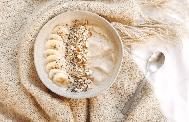 Light tan smoothie bowl with banana slices, seeds and other toppings.